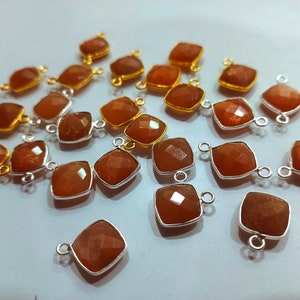 Può includere: Una collezione di 20 ciondoli in pietra preziosa marrone con accenti dorati e argentati. Ogni ciondolo presenta una pietra preziosa di forma quadrata con bordi sfaccettati. I ciondoli sono perfetti per la creazione di gioielli.