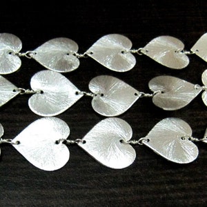 May include: A silver chain necklace with multiple heart-shaped links. The hearts are textured and have a brushed finish.