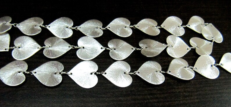 May include: A silver chain necklace with multiple heart-shaped links. The hearts are textured and have a brushed finish.