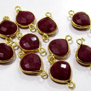 May include: Ten gold-plated teardrop-shaped gemstone connectors with a faceted ruby-colored stone. Each connector has two jump rings for attaching to jewelry.
