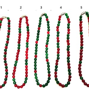 May include: Five necklaces made of alternating red and green beads. The necklaces are all the same length and have a silver clasp.