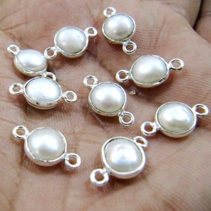 Puede incluir: Diez conectores de perlas blancas con bucles de metal plateados. Las perlas son redondas y lisas, y los bucles son de doble extremo.