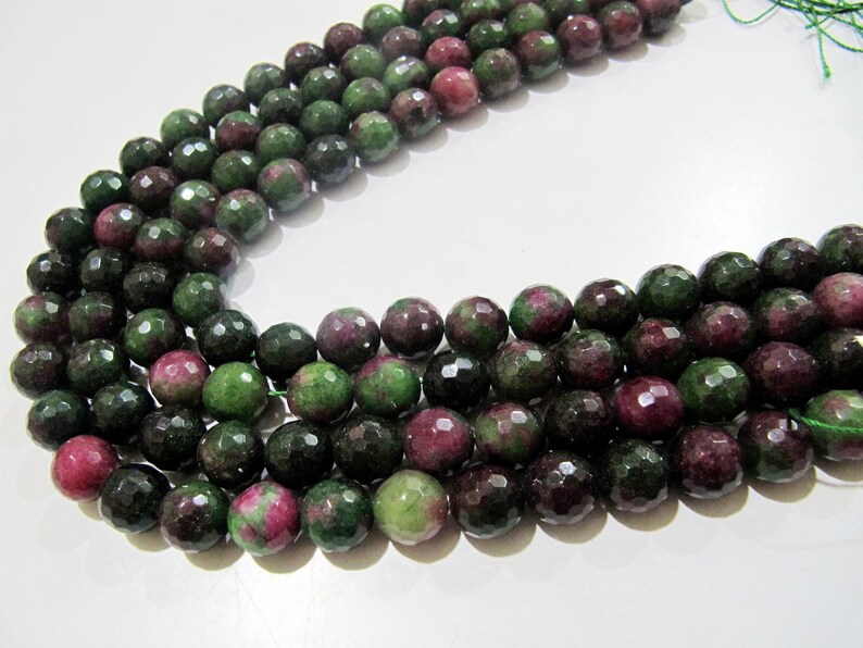 May include: A strand of faceted green and pink gemstone beads. The beads are round and have a polished finish.