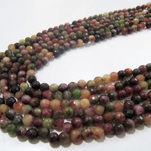 May include: Strands of faceted gemstone beads in various colours, including green, red, brown, and peach. The beads are round and have a polished, reflective surface. The beads are strung together, ready for jewellery making.