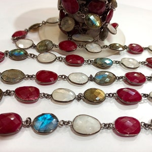 Può includere: Una catena d'argento con perline di pietre preziose rosse, bianche e iridescenti. La catena è composta da perline ovali collegate da anelli d'argento.