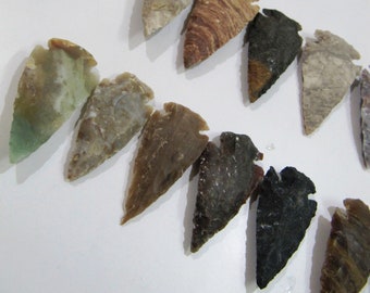 Puede incluir: Una colección de diez piedras en forma de punta de flecha en varios tonos de marrón, verde y gris. Las piedras son lisas y pulidas, con una variedad de patrones y texturas.