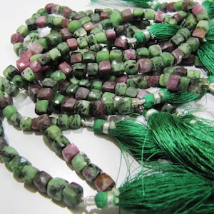 May include: A strand of green and pink gemstone beads with silver accents and green tassels. The beads are square shaped and have a faceted finish.
