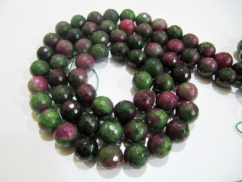 May include: A strand of faceted green and pink gemstone beads. The beads are round and have a polished finish.