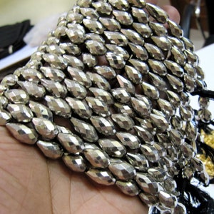 May include: A strand of silver-toned faceted teardrop beads. The beads are arranged in a row and are all the same size and shape.