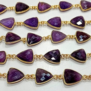Puede incluir: Una hebra de cuentas de piedra preciosa amatista conectadas por una cadena de oro. Las cuentas son de forma triangular y tienen un color morado intenso.