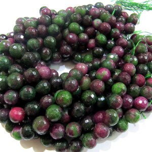 May include: A strand of faceted gemstone beads in shades of green and pink. The beads are round and have a smooth, polished finish.