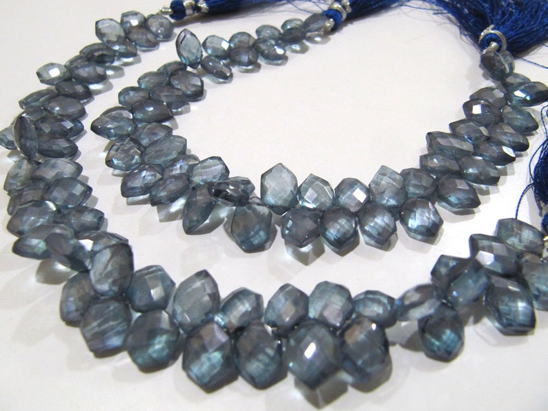 May include: A strand of faceted blue topaz beads, each bead is a unique, irregular shape. The beads are strung on a cord with a blue tassel at each end.