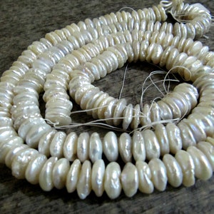 May include: Strands of lustrous, off-white, irregular-shaped pearls. The pearls are strung together, creating a coiled pattern. The pearls have a natural, organic appearance, suggesting they are freshwater pearls, perfect for jewelry making.