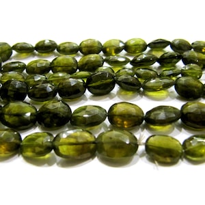 以下が含まれることがあります： 濃い緑色のファセットカットされた楕円形の宝石ビーズのストランド。ビーズは透明な糸に通されており、サイズは約10mmです。