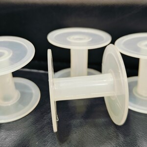 May include: Four clear plastic spools for thread or wire. The spools are stacked on top of each other.
