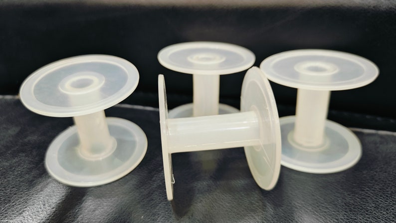 May include: Four clear plastic spools for thread or wire. The spools are stacked on top of each other.