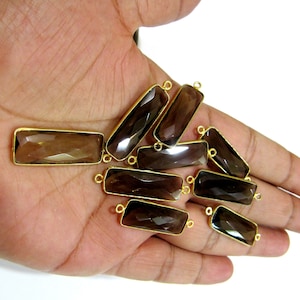 Peut inclure: Un groupe de pendentifs rectangulaires en pierre précieuse brune avec des anneaux de saut dorés. Les pendentifs sont facetés et ont une apparence translucide.