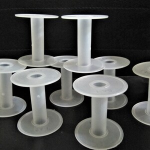 May include: Eight white plastic spools for thread or yarn. The spools are stacked on top of each other and have a smooth, round surface.