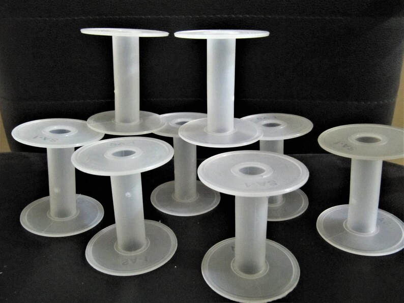 May include: Eight white plastic spools for thread or yarn. The spools are stacked on top of each other and have a smooth, round surface.