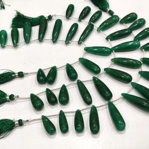 Peut inclure: Plusieurs brins de perles de pierres précieuses vertes polies en forme de goutte. Chaque brin est enfilé sur un fil fin et fini par un pompon vert. Les perles varient en taille et en forme, créant un aspect naturel. Idéal pour la création de bijoux.