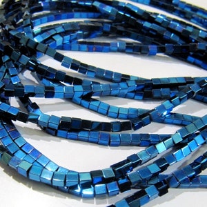 Può includere: Una collana di perline quadrate di colore blu scuro. Le perline hanno un effetto metallico e sono infilate su un filo trasparente.