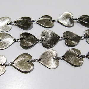 May include: A silver necklace with a chain made of small metal hearts. The hearts are connected by small silver rings.