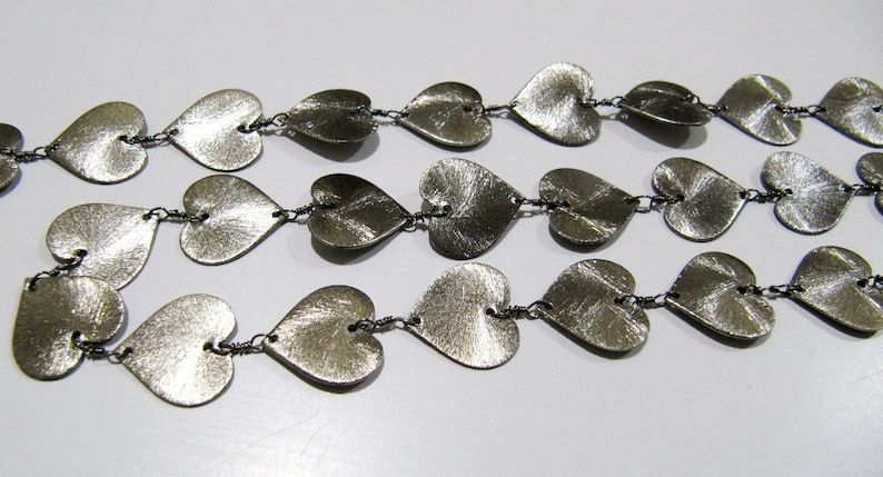 May include: A silver necklace with a chain made of small metal hearts. The hearts are connected by small silver rings.