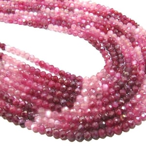 May include: A strand of pink and red faceted gemstone beads. The beads are round and have a smooth, polished finish.