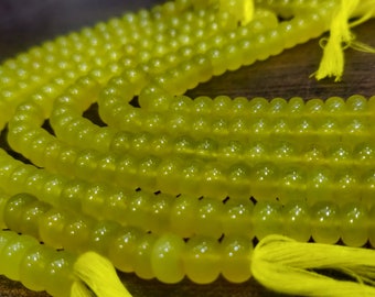 May include: A strand of bright yellow beads, likely made of glass or gemstone, with yellow tassels at the ends. The beads are round and smooth, and the strand is coiled on a wooden surface.