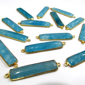 May include: A group of 14 turquoise blue gemstone rectangle pendant connectors with gold-toned metal accents. The connectors have a smooth, polished finish and are perfect for jewelry making.