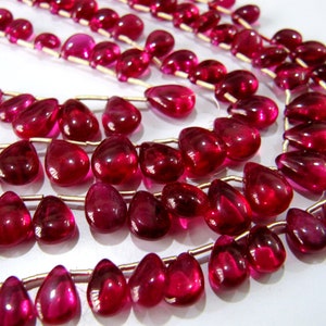 May include: A strand of bright red gemstone beads in a teardrop shape. The beads are strung on a silver wire.