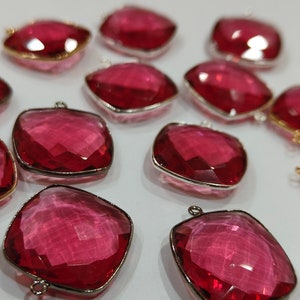 May include: Twelve pink faceted gemstone pendants with gold-toned metal accents. The pendants are square-shaped and have a shiny, translucent finish.