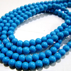 May include: Strands of bright turquoise beads. The beads are round and have a glossy finish. The beads are strung together, forming multiple strands. The beads are a vibrant blue color, perfect for jewelry making or crafting.