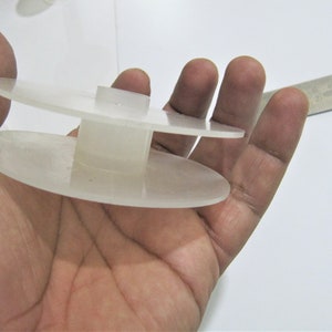 May include: A white plastic spool with two circular discs and a central cylinder. The spool is designed to hold thread or yarn.