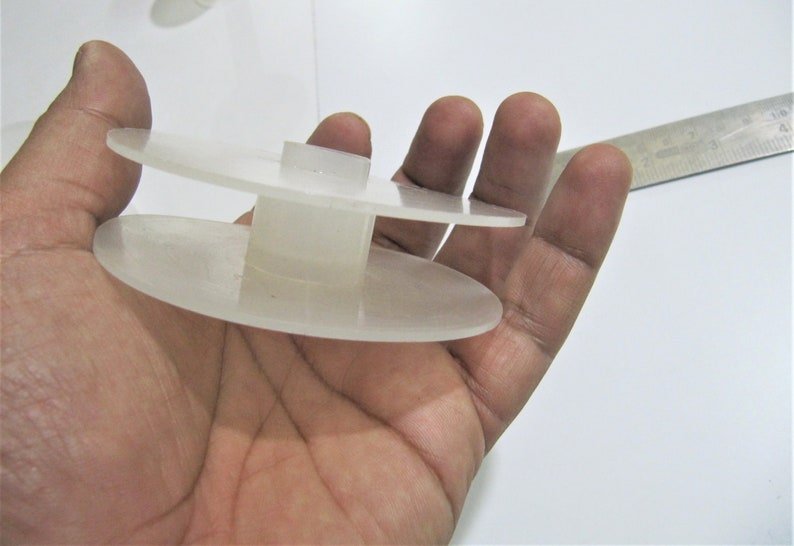 May include: A white plastic spool with two circular discs and a central cylinder. The spool is designed to hold thread or yarn.