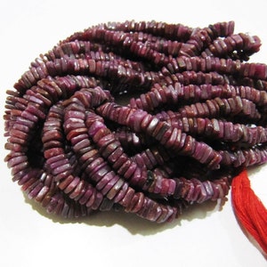 Puede incluir: Una hebra de cuentas de rubí púrpura, cada cuenta es rectangular y tiene una forma ligeramente irregular. Las cuentas están enhebradas en un hilo rojo.