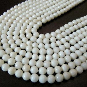May include: A strand of white round beads made from natural shell. The beads are smooth and polished, with a slight variation in color and texture.