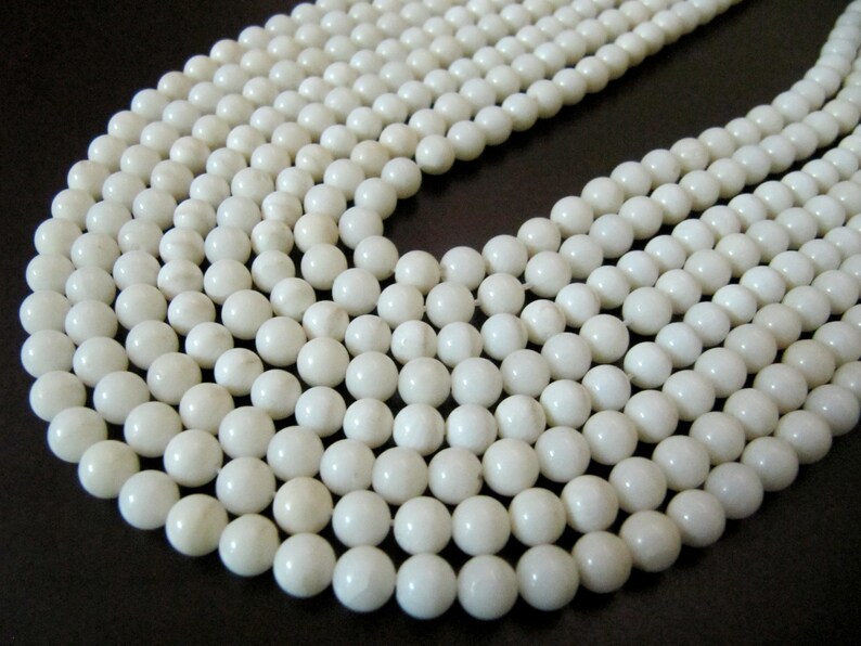 May include: A strand of white round beads made from natural shell. The beads are smooth and polished, with a slight variation in color and texture.