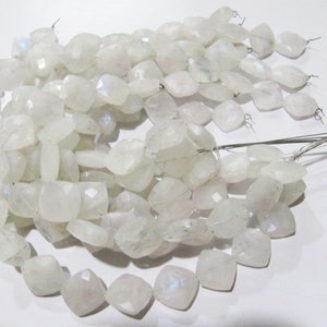 Puede incluir: Una hebra de cuentas de piedra lunar blanca con forma cuadrada. Las cuentas están enhebradas en alambre y tienen un brillo iridiscente.