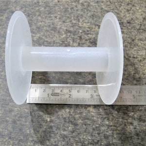 May include: A white plastic spool with a 3-inch diameter. The spool is used for winding thread or yarn.