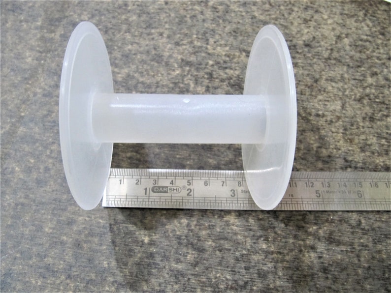 May include: A white plastic spool with a 3-inch diameter. The spool is used for winding thread or yarn.