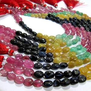 May include: A strand of oval-shaped gemstone beads in various colours, including pink, green, yellow, and blue. The beads are strung on a cord and have a tassel at each end.
