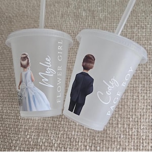 May include: Two clear plastic cups with lids and straws. One cup features a drawing of a flower girl in a blue dress, the name "Mylie", and the text "Flower Girl". The other cup has a drawing of a page boy in a suit, the name "Cody", and the text "Page Boy".