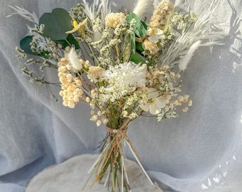 Op de afbeelding: Een boeket droogbloemen met witte hortensia's, crèmekleurig gipskruid, pluizig wit pampasgras, groene eucalyptusbladeren en kleine witte bloemetjes. De stelen zijn samengebonden en vastgezet met een dun bruin touwtje.