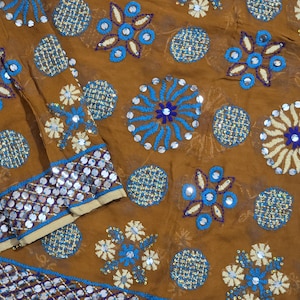 Könnte beinhalten: Ein brauner Stoff mit einem komplizierten Muster aus gestickten kreisförmigen Motiven in Blau, Creme und Dunkelviolett. Das Design enthält kleine reflektierende Pailletten in der Stickerei und einen Rand mit Reihen silberner Pailletten.