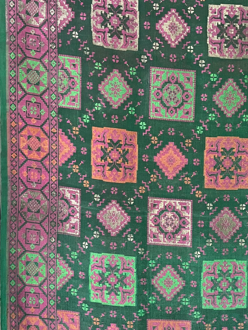 May include: A green fabric with a repeating pattern of pink, orange, and silver geometric shapes. The fabric has a border with a more intricate design.