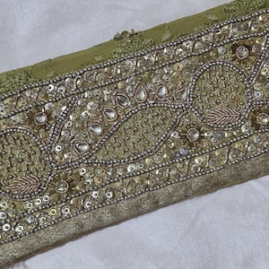 May include: An olive green fabric border featuring intricate hand embroidery with silver beads, clear sequins, and metallic thread. The design includes repeating circular and leaf-shaped patterns accented with small reflective stones.
