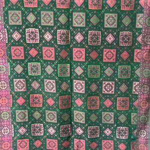 May include: A green fabric with a repeating pattern of pink, green, and gold squares. The fabric has a subtle sheen and a soft texture.