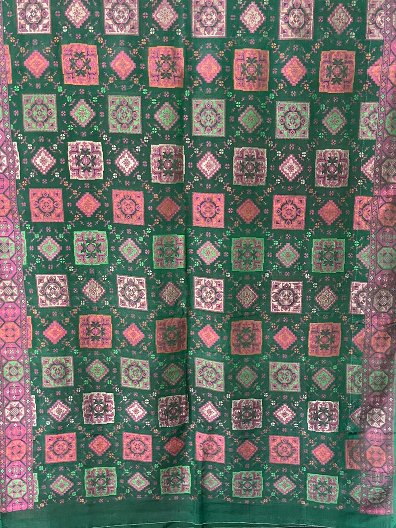 May include: A green fabric with a repeating pattern of pink, green, and gold squares. The fabric has a subtle sheen and a soft texture.