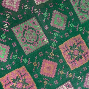 May include: Green fabric with a repeating pattern of pink, orange, and green squares. The squares have a geometric design.
